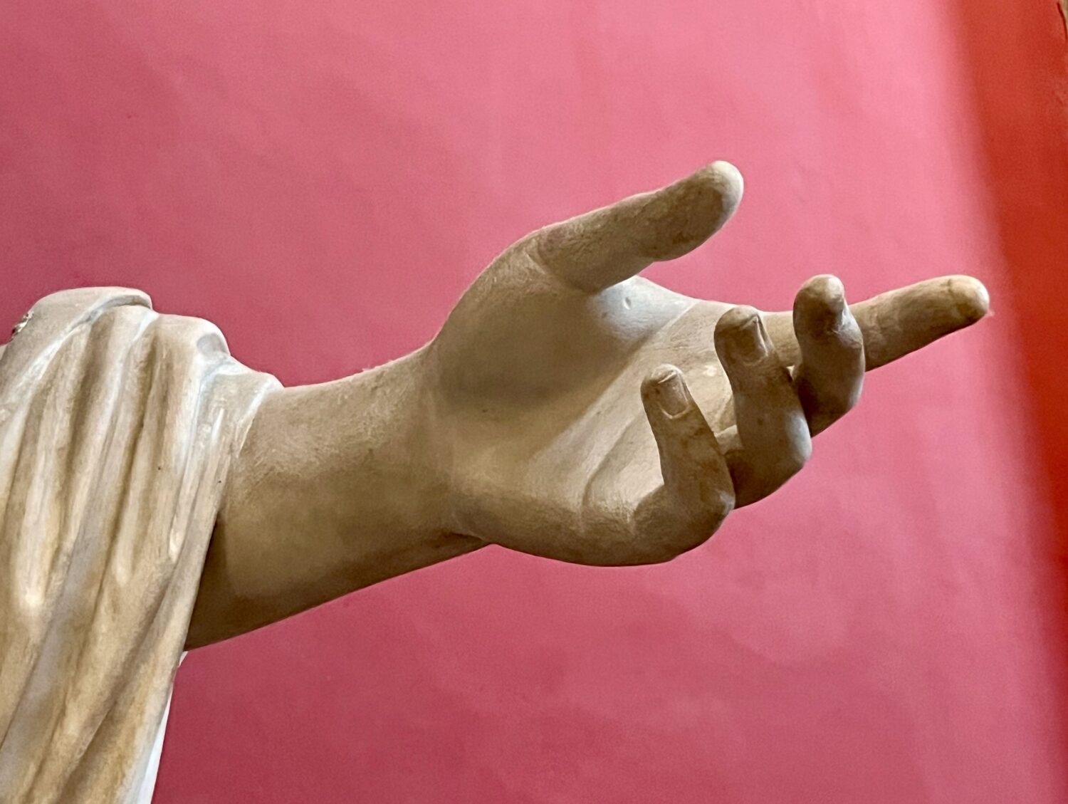 Utsträckt hand mot röd bakgrund tillhörande en staty i Vatikanen