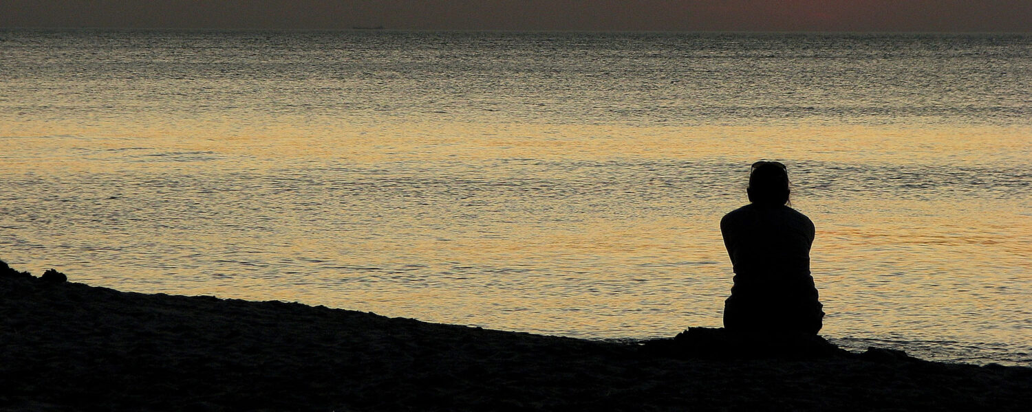 människa som blickar ut över hav i kvällsjjus